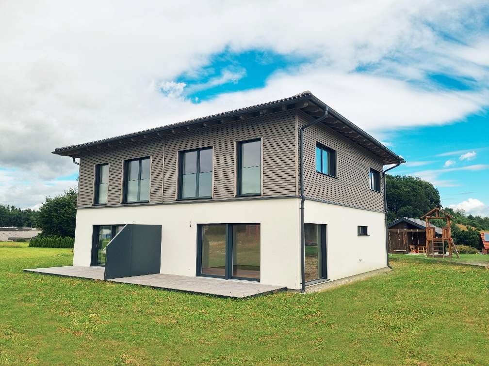 grau/weiße Doppelhaushälte mit Terrasse und Rasenfläche.